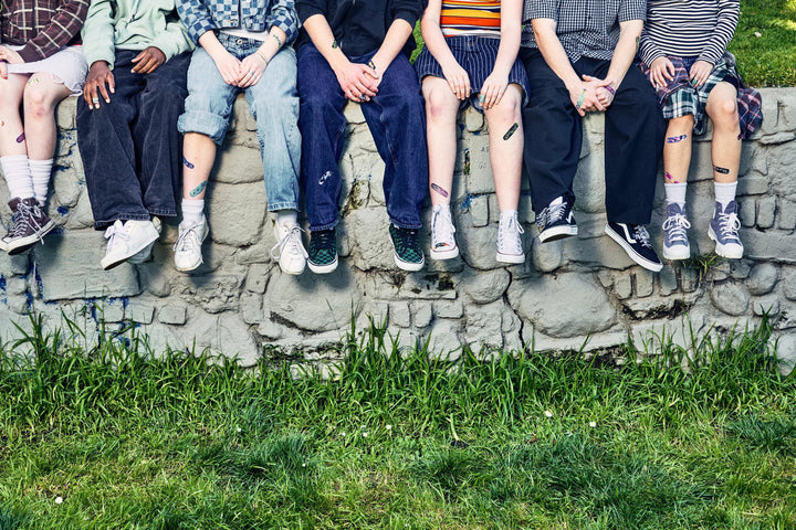 Row of teens sitting on a stone wall with their legs over the grass, several wearing World of Hurt bandages on their knees