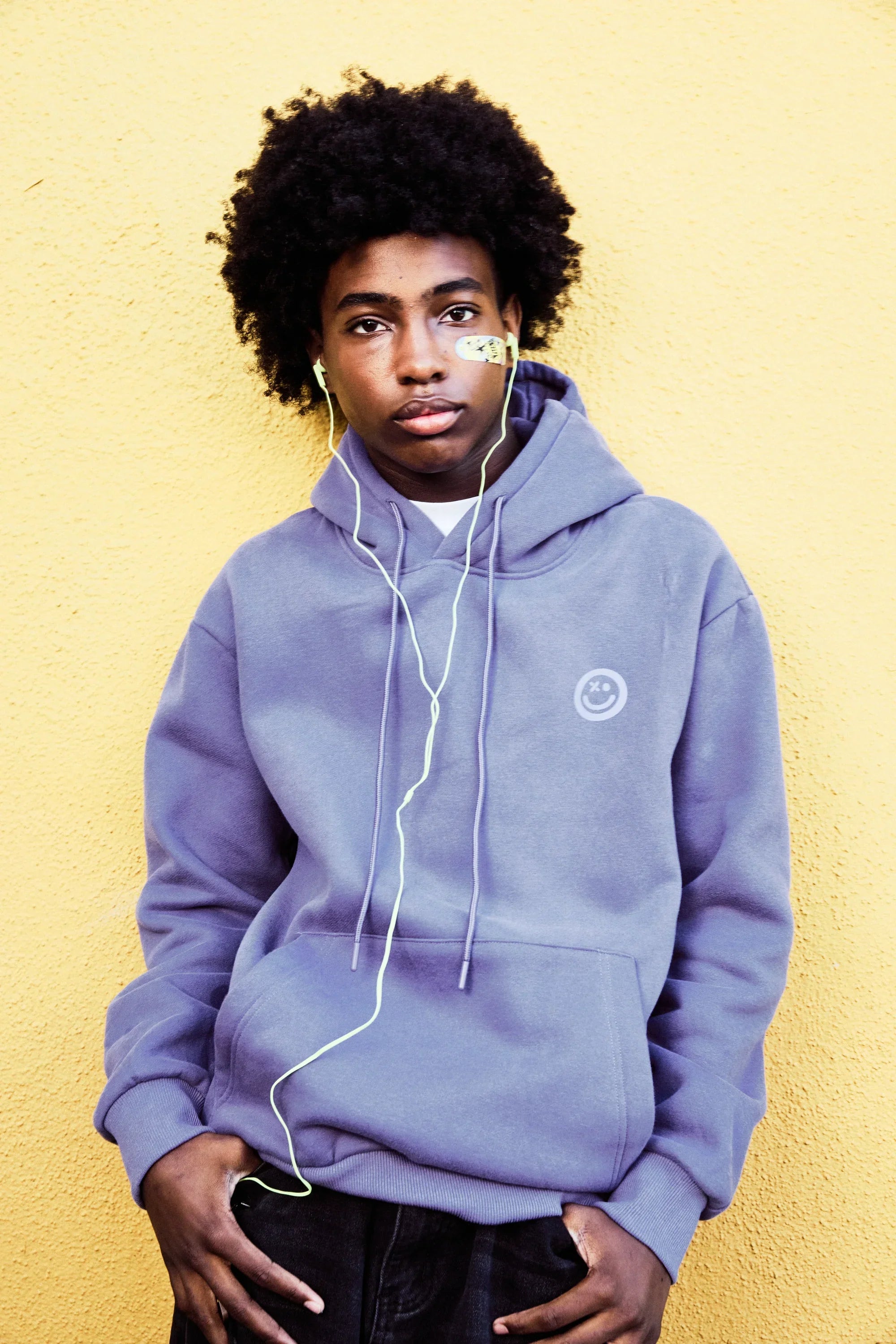 Teen against a yellow wall wearing a World of Hurt bandage near the eye