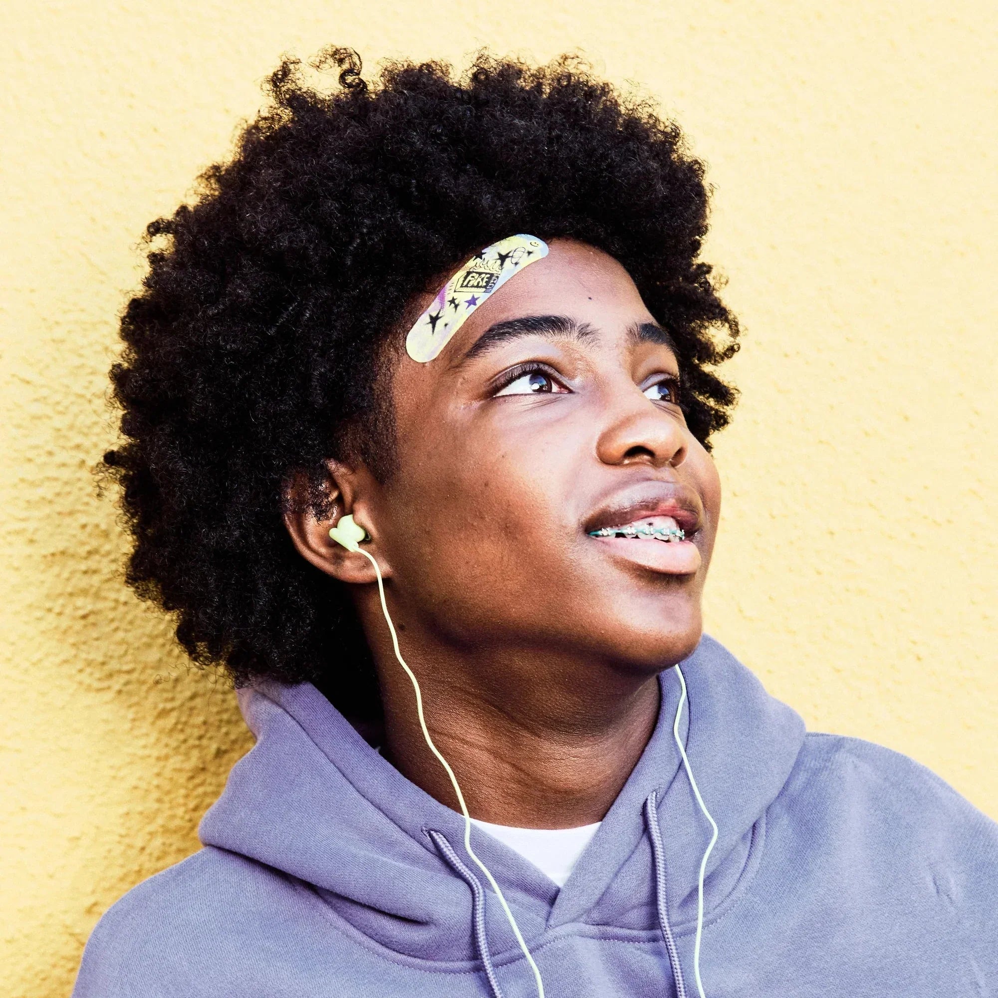 Young man wearing a World of Hurt decorative bandage on his face, yellow background