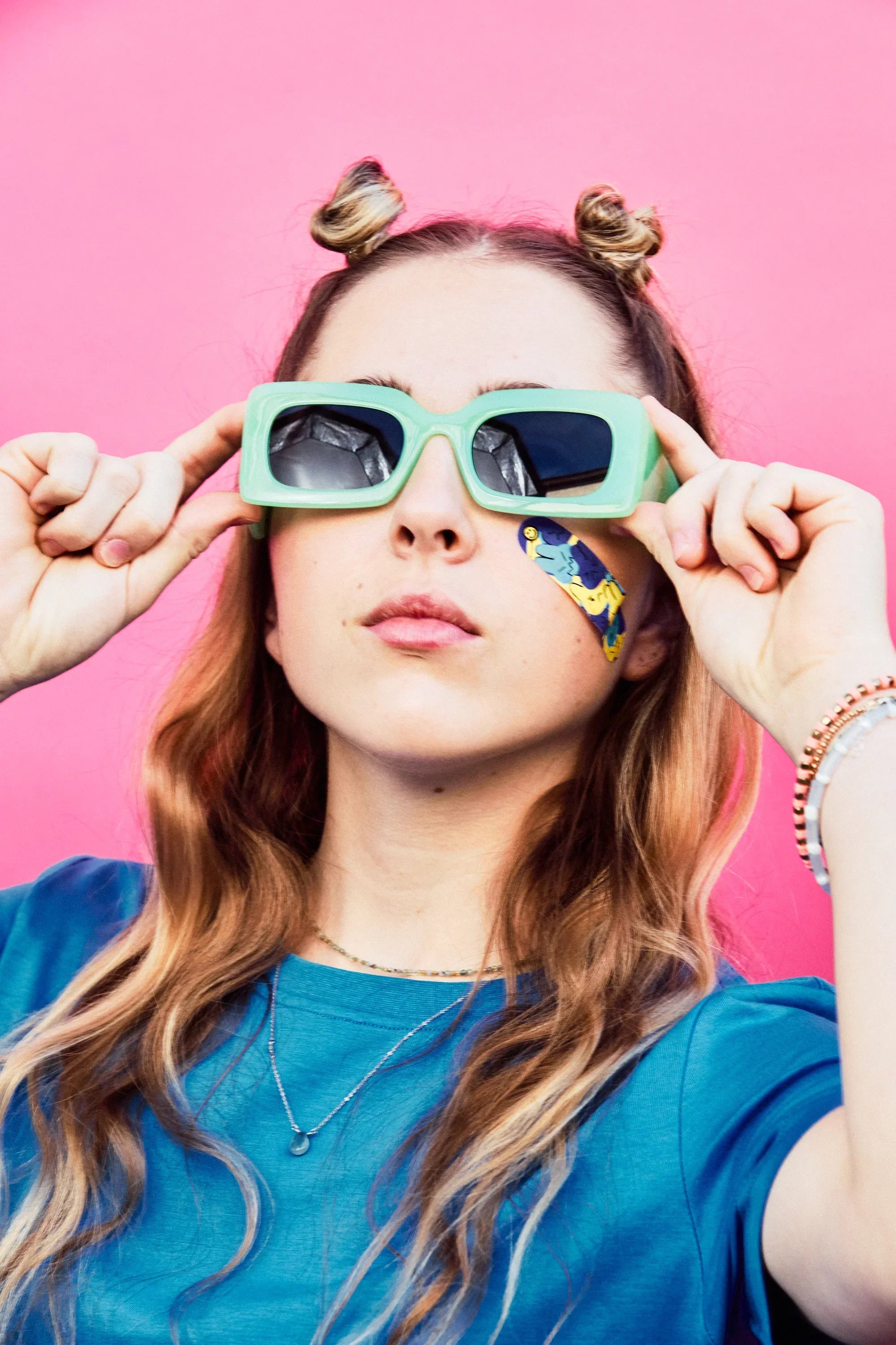 Teen in sunglasses wearing World of Hurt decorative bandages on the cheek